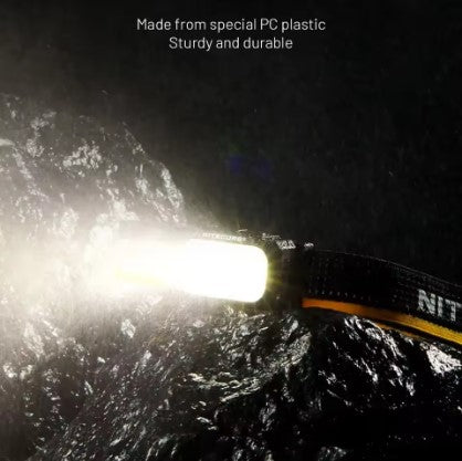 Night scene photo with mountains in background, showing NU25 MCT headlamp made from special PC plastic glowing brightly in dark environment. Demonstrates sturdy build and high luminous output.