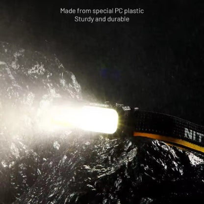 Night scene photo with mountains in background, showing NU25 MCT headlamp made from special PC plastic glowing brightly in dark environment. Demonstrates sturdy build and high luminous output.